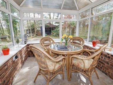A conservatory with a round glass table and four wicker chairs with cushions at The Old Barn in Llanferres near Ruthin