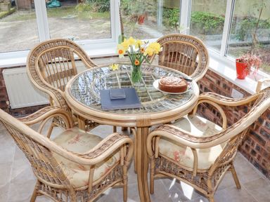 A glass top table with a cake flowers and notebooks surrounded by four wicker chairs in a sunroom at The Old Barn in Llanferres near Ruthin