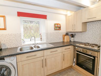 A kitchen with a double sink under a window with a red blind and light wood cabinets at The Old Barn in Llanferres near Ruthin