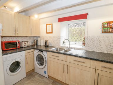 A kitchen with washing machines a sink window and cabinets at The Old Barn in Llanferres near Ruthin