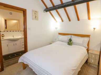 A bedroom with a double bed two bedside cabinets wall lights exposed ceiling beams and an adjoining bathroom at The Old Barn in Llanferres near Ruthin