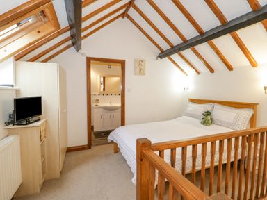 A bedroom with exposed wooden beams a bed a wardrobe a small tv and an ensuite bathroom at The Old Barn in Llanferres near Ruthin