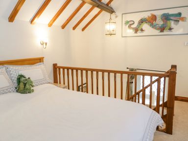 A bedroom with a bed and stuffed dragons next to a wooden railing and a dragon painting on the wall at The Old Barn in Llanferres near Ruthin