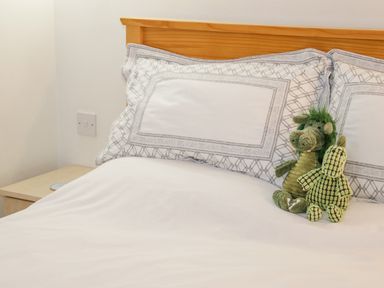 A bedroom with a wooden bed frame two pillows with patterned pillowcases two stuffed animal toys on the bed at The Old Barn in Llanferres near Ruthin