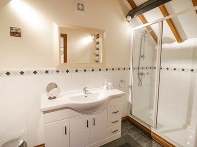 A bathroom with a sink vanity and mirror next to a glass shower at The Old Barn in Llanferres near Ruthin