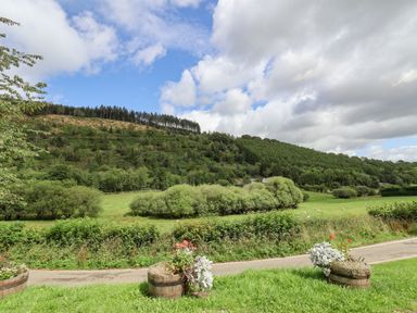 A rural landscape with grassy fields bushes and trees under a partly cloudy sky at The Old Barn in Llanferres near Ruthin