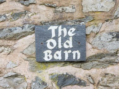 A stone wall with a black sign that reads The Old Barn at The Old Barn in Llanferres near Ruthin