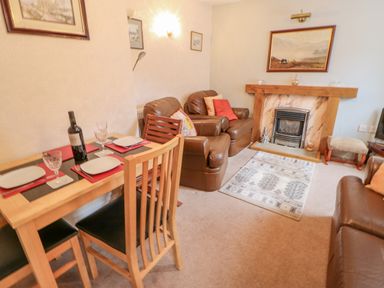 A living room with a dining table set for two and leather armchairs near a fireplace at Blacksmith Cottage in Appleby-in-Westmorland