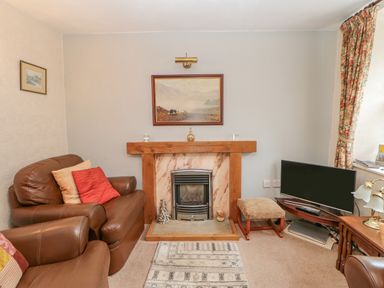 A living room with a fireplace leather sofas a small television on a stand and floral curtains at Blacksmith Cottage in Appleby-in-Westmorland