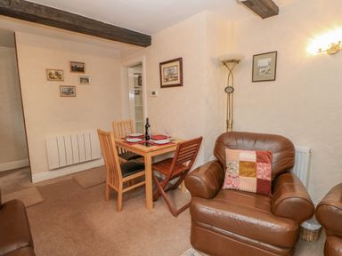 A living room with a wooden dining table set with plates and glasses and brown leather armchairs at Blacksmith Cottage in Appleby-in-Westmorland