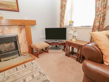 A corner of a living room with a fireplace TV stool side tables lamp and a leather armchair at Blacksmith Cottage in Appleby-in-Westmorland