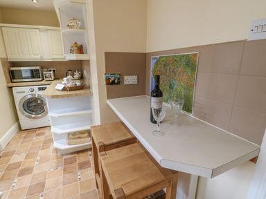 A kitchen area with a washing machine microwave countertop with wine bottle and glasses at Blacksmith Cottage Appleby-in-Westmorland