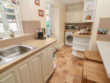 A kitchen with a sink kettle washing machine microwave and shelves at Blacksmith Cottage in Appleby-in-Westmorland