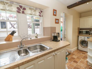 A kitchen with a double stainless steel sink a knife block a kettle a microwave and a washing machine at Blacksmith Cottage in Appleby-in-Westmorland