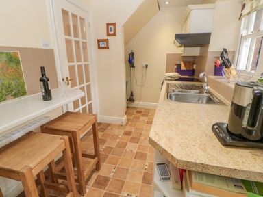 A kitchen with wooden stools a wine bottle on a counter a stainless steel sink and an air fryer at Blacksmith Cottage in Appleby-in-Westmorland