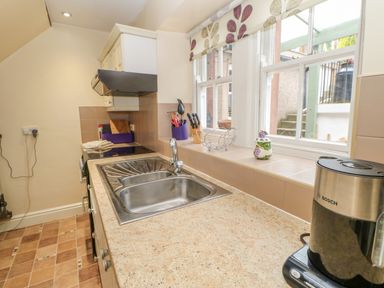 A kitchen sink with a faucet on a countertop next to a coffee maker and utensils under a window at Blacksmith Cottage in Appleby-in-Westmorland