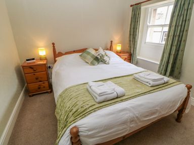 A bedroom with a wooden bed white bedding two bedside tables with lamps and a window with curtains at Blacksmith Cottage in Appleby-in-Westmorland