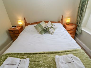 A bedroom with a wooden bed frame green cushions bedside tables with lamps and folded towels at Blacksmith Cottage in Appleby-in-Westmorland