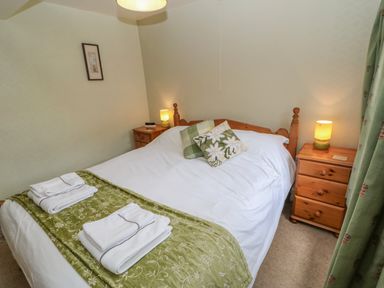 A bedroom with a double bed with white and green bedding two bedside tables with lamps and folded towels on the bed at Blacksmith Cottage in Appleby-in-Westmorland