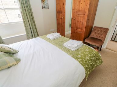 A bedroom with a bed, wooden wardrobe, chair, and window with curtains at Blacksmith Cottage in Appleby-in-Westmorland