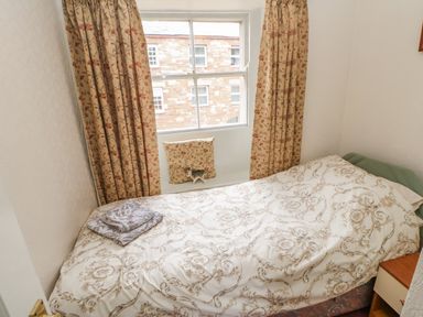 A small bedroom with a bed covered in patterned bedding and folded towels by a window with floral curtains at Blacksmith Cottage Appleby-in-Westmorland