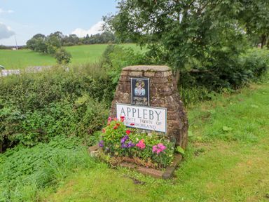 A stone town sign with flowers and green fields in the background at Blacksmith Cottage in Appleby-in-Westmorland