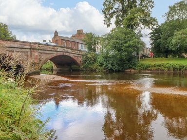 A stone bridge over a river with trees and buildings in the background at Blacksmith Cottage in Appleby-in-Westmorland