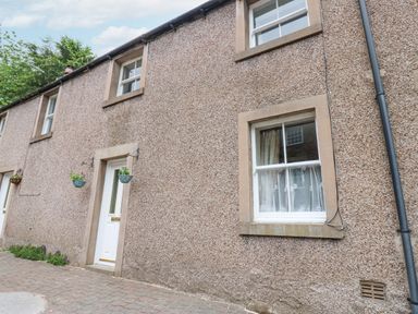 Exterior of a stone house with white doors and windows with hanging flower baskets at Blacksmith Cottage in Appleby-in-Westmorland