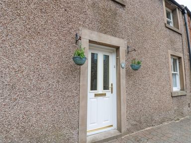 A white front door with two hanging baskets on a pebble dash wall at Blacksmith Cottage in Appleby-in-Westmorland