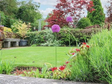 A garden with green grass purple and red flowers plants and a stone bench at Blacksmith Cottage in Appleby-in-Westmorland