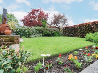 A garden with a green lawn various shrubs flowers and a rusted chiminea at Blacksmith Cottage in Appleby-in-Westmorland