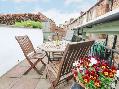 A balcony with wooden table and chairs wine glasses and flowers at Blacksmith Cottage in Appleby-in-Westmorland
