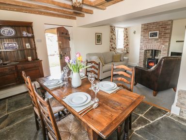 A dining table set with plates and glasses next to a wooden cupboard and a seating area with sofa and armchair near a fireplace at Bears Cottage in Bretforton near Broadway