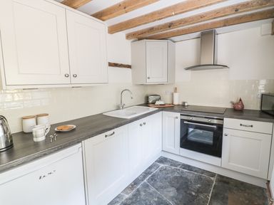 A kitchen with white cabinets gray countertops a sink oven stovetop toaster and wooden ceiling beams at Bears Cottage in Bretforton near Broadway