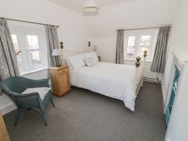 A bedroom with a bed two bedside tables two windows curtains a blue chair and a fireplace at Bears Cottage in Bretforton near Broadway