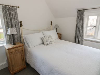 A bedroom with a double bed white bedding wooden bedside tables lamps and grey curtains at Bears Cottage in Bretforton near Broadway