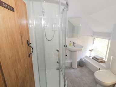 A bathroom with a glass shower cubicle a white sink a toilet folded towels on a windowsill and a wooden door at Bear's Cottage in Bretforton near Broadway