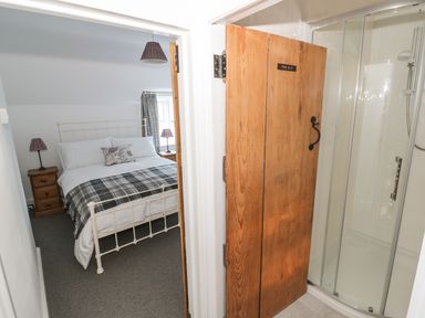A bedroom with a double bed next to a bathroom with a wooden door and shower at Bear's Cottage Bretforton near Broadway