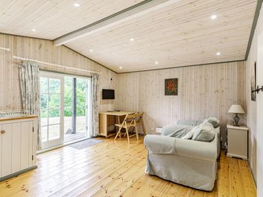 A room with two armchairs a small table and chairs a wall mounted television and sliding glass doors at Lakeside Cabin in Sheldon Blackdown Hills