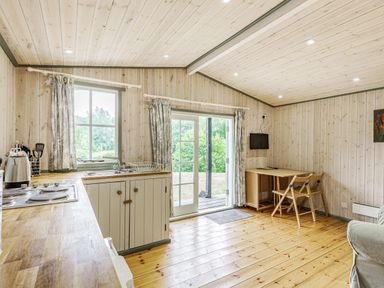A kitchen and dining area with wooden floors and walls and a table with chairs at Lakeside Cabin in Sheldon Blackdown Hills