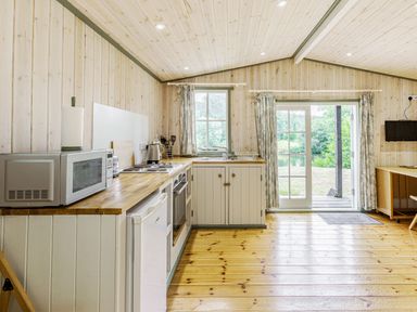 A kitchen with wooden countertops white cabinets a microwave fridge and a window and glass door at Lakeside Cabin in Sheldon Blackdown Hills