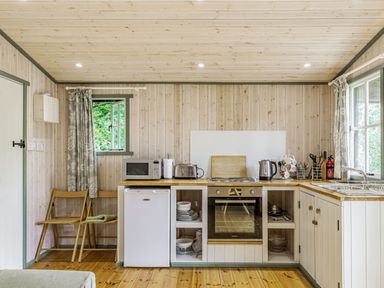 A kitchen with wooden walls and floor two folding chairs countertop appliances an oven and a sink at Lakeside Cabin in Sheldon Blackdown Hills