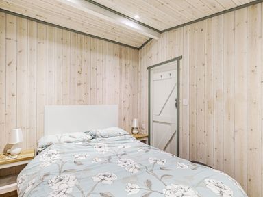 A bedroom with a bed with floral bedding and wood paneled walls at Lakeside Cabin in Sheldon Blackdown Hills