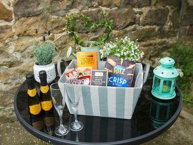 A round glass table with two small bottles of prosecco two champagne glasses a basket with snacks and plants a green lantern and a potted plant at West Wing Cottage in Hexham