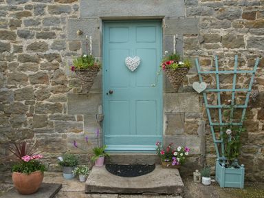 A stone wall with a blue door decorated with hanging baskets and potted plants at West Wing Cottage in Hexham