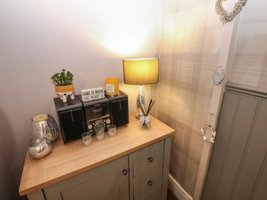 A wooden cabinet with a lamp plant radios candles and decorative hearts on the wall at West Wing Cottage in Hexham