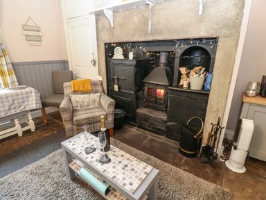 A living room with a fireplace wood stove armchairs a coffee table with glasses and a bottle and a rug at West Wing Cottage in Hexham