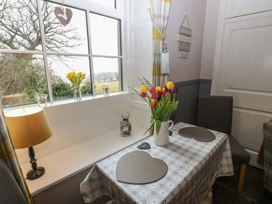 A dining table with flowers and heart shaped mats by a window with a lamp at West Wing Cottage in Hexham