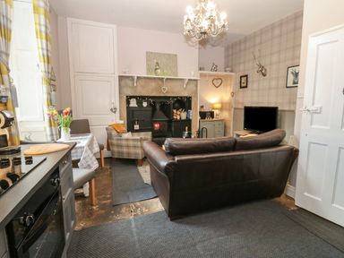 A living room with a brown leather sofa a plaid armchair a fireplace and a television at West Wing Cottage in Hexham