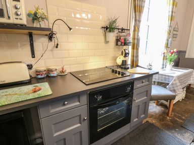 A kitchen with a stovetop oven toaster jars and a dining table with flowers at West Wing Cottage in Hexham